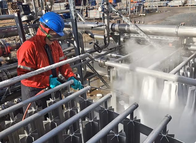 Arbeiter in Schutzhelm, Schutzbrille und Handschuhen bedient eine industrielle Anlage mit dampfendem Gas oder Dampf.