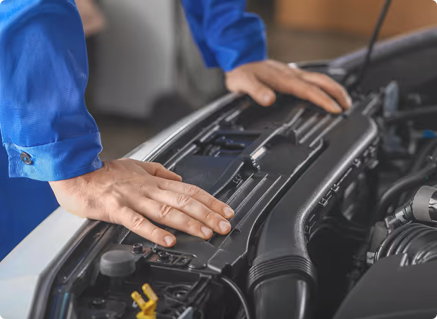 Mechaniker prüft mit beiden Händen den Motorraum eines Autos.