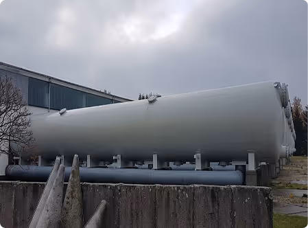 Große weiße Zylinder, die auf Stützen im Freien vor einem Industriegebäude stehen.